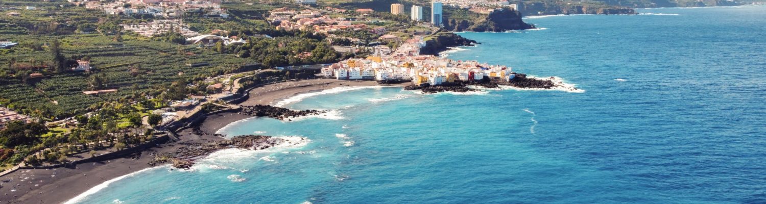 Aerial drone view of Puerto de la Cruz in Tenerife, Canary Islands. Multiple residential buildings, Atlantic ocean rocky coast with hills on the island